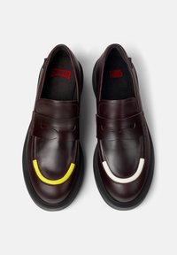 Bruine leren loafers met een dikke zwarte zool, voorzien van gele en witte accenten aan de voorkant voor extra detail. Rode binnenbranding.