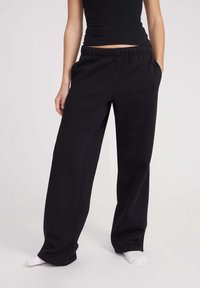 Schwarze, weit geschnittene Sweatpants mit einem elastischen Bund und Taschen an der Seite. Weicher, strukturiertes Material; schmal zulaufendes Beinende; minimale Nähte.