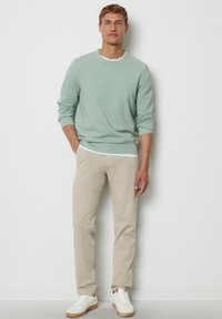 Hellgrüner Strickpullover mit gerippten Bündchen, kombiniert mit beige schlanken Hose und weißen Sneakern mit Gummisohle.