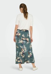 Maxi nederdel i grøn med blomstermønster, lavet af blødt stof. Har en samlet talje og flydende design, parret med en ensfarvet hvid top.