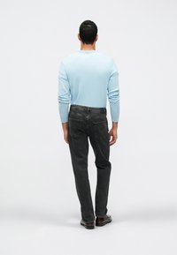 Top de manga longa azul claro e jeans cinza escuro, vistos de trás. Os jeans possuem bolsos traseiros e um acabamento texturizado.