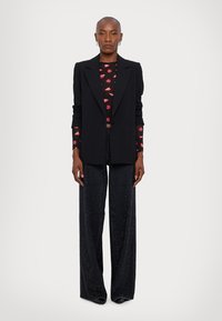 Black tailored blazer over a black shirt with red lip pattern, paired with wide-leg black pants featuring sparkly embellishments.