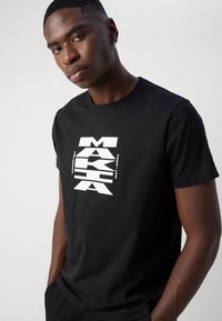 Svart bomulls T-skjorte med en iøynefallende hvit grafisk design med tekst. Korte ermer og rund hals. Sømløst stoff med en avslappet passform.