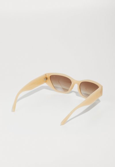 Beige plastic sunglasses with a cat-eye shape, gradient brown lenses, and slender arms featuring a gold accent detail near the hinge.