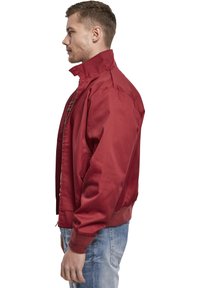 Veste bombardier rouge avec un col haut, des poches latérales et des poignets côtelés. Fabriquée en tissu durable avec une texture lisse.