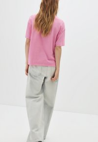Roze oversized t-shirt met korte mouwen, gecombineerd met losse lichtgrijze jeans. Opvallende zakdetails op de jeans.