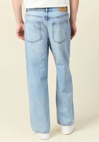 Ljusblå denimjeans med lös passform, femficksdesign och synlig sömnad. Har en beige etikett på den bakre midjan.