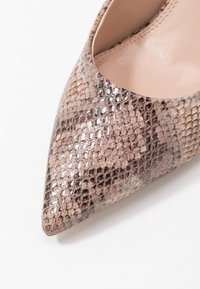 Lodička s špičatou špičkou vyrobená z texturovaného kovového materiálu se vzorem hadí kůže v odstínech hnědé a bronzové, s hladkým tělovým interiérem.