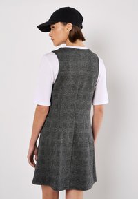 Vestido a cuadros gris con forma ajustada y falda acampanada. Incluye una camiseta blanca por debajo y una gorra negra. Tela texturizada con costuras visibles.