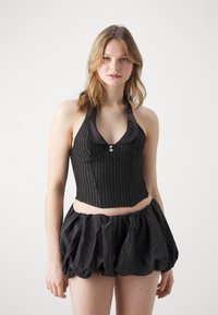 Black striped crop top with a satin collar and button detail, paired with a voluminous black ruffled skirt, offering texture contrast.