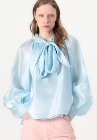 Blusa di satinazzurro chiaro con colletto a fiocco, maniche a palloncino e polsini arricciati. Texture morbida con una vestibilità comoda.