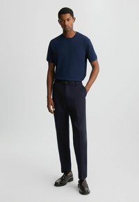 Marinblå crew-neck t-shirt kombineret med skræddersyede mørke bukser. Outfittet har rene linjer og en moderne pasform. Sorte sko fuldender looket.
