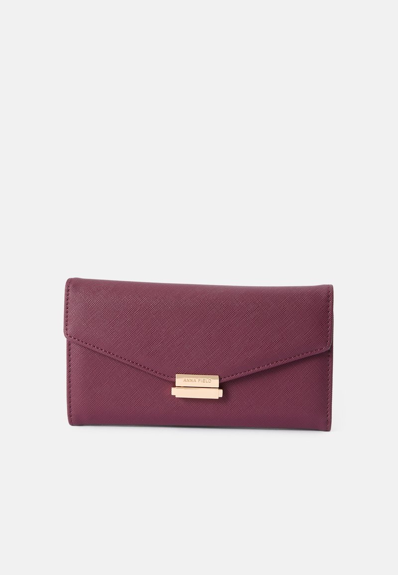 Burgundy väärennöstä nahkaa oleva lompakko, jossa on teksturoitu pinta. Varustettu kultaisella sulkimella ja kohokuvioidulla brändin nimellä edessä. Kolmion muotoinen läppädesign.