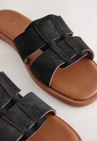 Sandales en daim noir à deux larges brides, présentant une semelle intérieure lisse couleur tan et une semelle extérieure en caoutchouc épaisse pour une durabilité accrue.