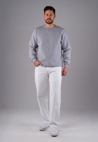 Grauer Pullover mit langen Ärmeln, Rundhalsausschnitt und gerippten Bündchen. Kombiniert mit weißen Jeans und weißen Sneakers. Schlichtes Design, keine Muster.