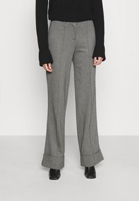 Pantalones de pierna ancha grises con detalles cosidos y puños, fabricados en una tela texturizada, combinados con un suéter negro de canalé. Zapatos negros visibles.