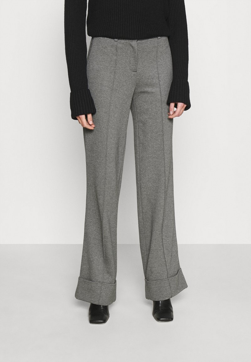 Pantalones de pierna ancha grises con detalles cosidos y puños, fabricados en una tela texturizada, combinados con un suéter negro de canalé. Zapatos negros visibles.