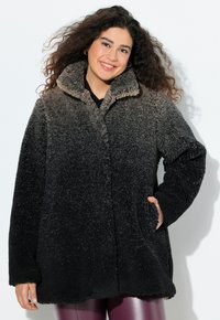 Mustan ja ruskean sävyinen fleece-takki, jossa on korkea kaulus, teksturoitu pinta ja sivutaskut. Pitkät hihat ja pehmeä rakenne.