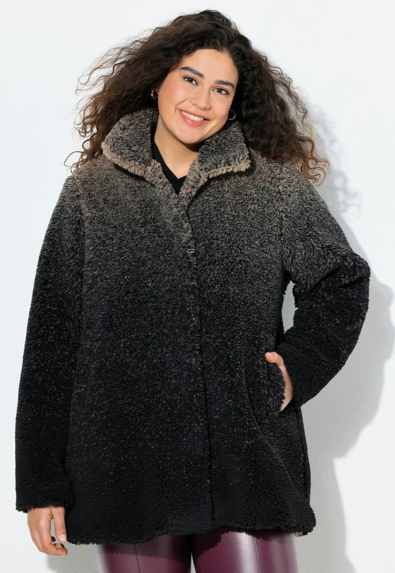 Mustan ja ruskean sävyinen fleece-takki, jossa on korkea kaulus, teksturoitu pinta ja sivutaskut. Pitkät hihat ja pehmeä rakenne.