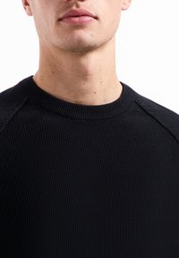 Schwarzer Strickpullover mit geripptem Muster, Rundhalsausschnitt und Raglanärmeln. Der Stoff wirkt dick und warm, ideal für kühleres Wetter.