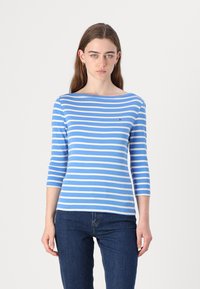 Blauw-wit gestreepte lange mouwtop met een bootnek en geborduurd logo op de borst, gecombineerd met donkerblauwe jeans.