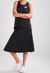 Černý bezramínkový top s bílým logem doplněný o černou sukně ke kolenům z texturované látky a bílé tenisky.
