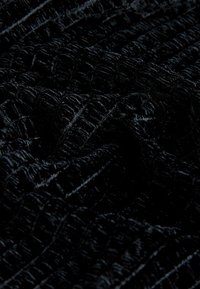 Čierna textúrovaná tkanina s vyvýšeným vzorom, ktorá má mäkký, plyšový vzhľad. Materiál vyzerá hladko a lákavo.