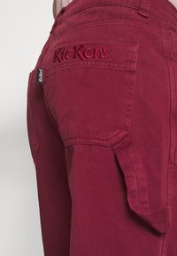 Bordeauxfarbene Baumwollhosen mit gesticktem "Kickers"-Logo, seitlichen Taschen und einer maßgeschneiderten Passform. Der Stoff hat eine glatte Textur mit stabilen Nähten.