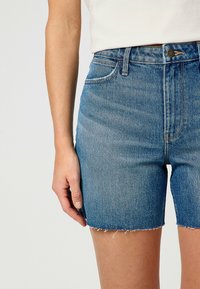 Vaaleansiniset farkkuhousut, joissa on kuluneet reunat, viisi taskua ja korkea vyötärö. Materiaali antaa luonnollisen, rentoutuneen tekstuurin.