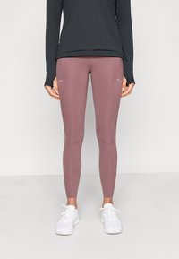 Leggings roses avec une texture lisse et une coupe ajustée, associés à un haut noir à manches longues. Des baskets blanches complètent la tenue.
