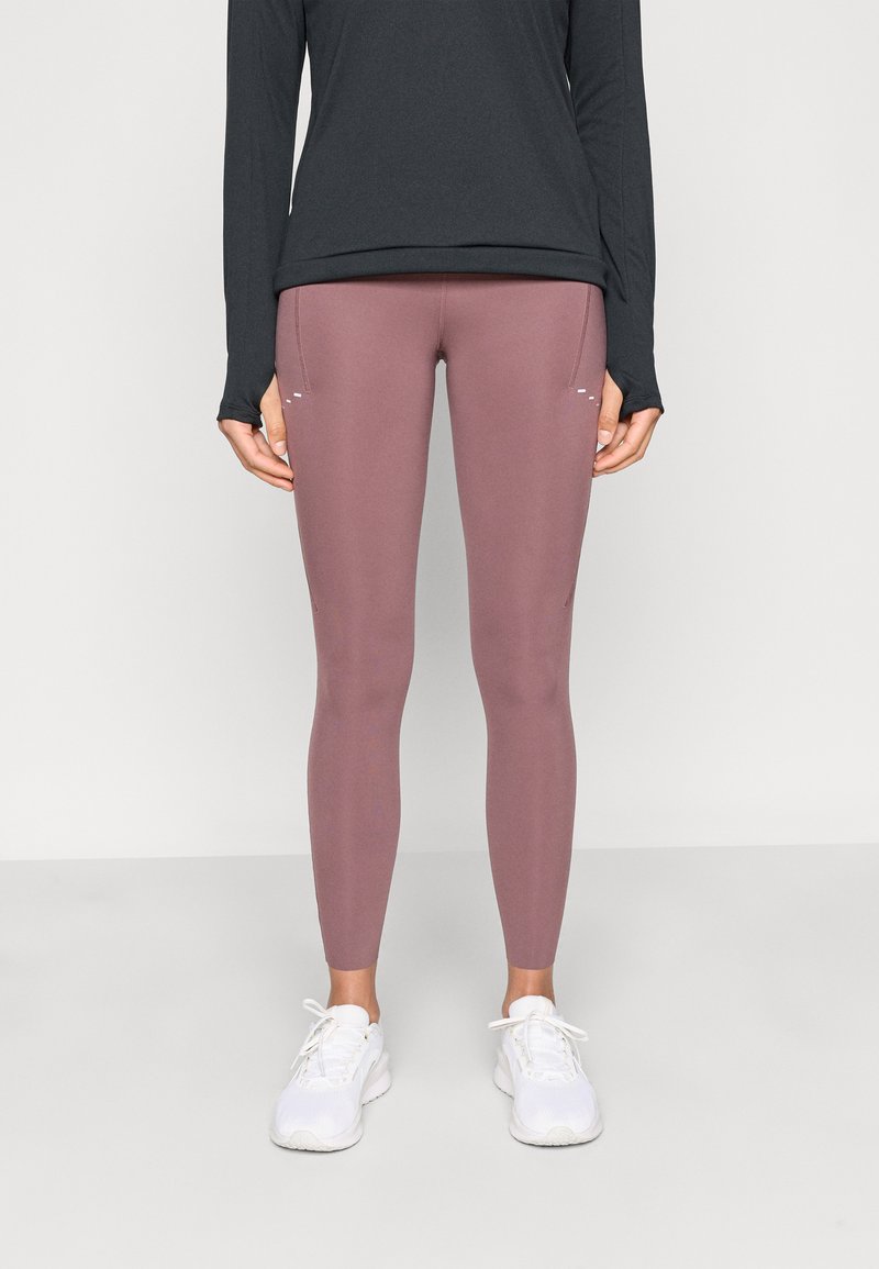 Leggings roses avec une texture lisse et une coupe ajustée, associés à un haut noir à manches longues. Des baskets blanches complètent la tenue.