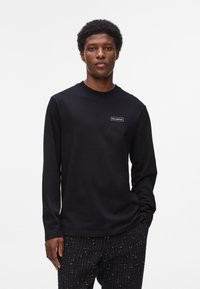 Sort langærmet T-shirt med rund hals i blødt stof, har et lille rektangulært logo på brystet og en afslappet pasform.