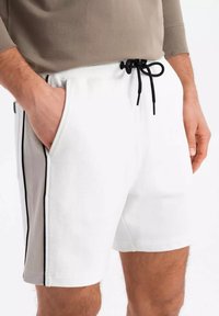 Shorts en coton blanc avec une coupe décontractée, dotés d'une taille avec cordon de serrage et de bandes noires sur les côtés le long des poches. Texture lisse.