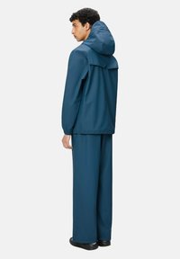 Set di giacca e pantaloni impermeabili in teal scuro, dotato di cappuccio, polsini elasticizzati e vestibilità comoda per libertà di movimento.
