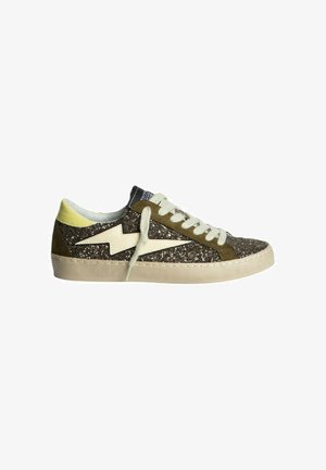 Zapatilla con un acabado brillante en marrón oscuro, acentos de ante verde oliva, cordones crema y una suela de goma beige con un diseño de rayo.