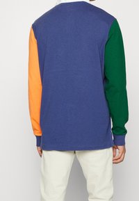 Långärmad skjorta med en marinblå kropp, orange vänsterärm och grön högerärm. Bomullsmaterial med ribbade manschetter. Avslappnad passform.