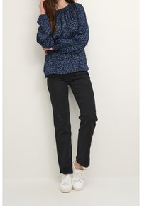 Blue leopard-print long-sleeve shirt with gathered neckline, paired with black skinny jeans and white sneakers.