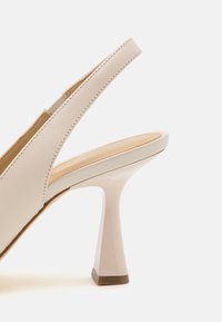 Sandal con tacco beige caratterizzato da un design elegante, materiale in pelle liscia e un tacco triangolare distintivo con finitura lucida.