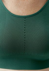 Zelená sportovní podprsenka z texturované žebrované látky, s bezešvým designem a dekorativním švem podél přední části.