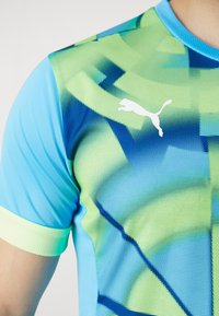 Jersey deportivo de Puma con textura de malla, vibrante combinación de colores azul y verde, patrones geométricos y un logo blanco de Puma en el pecho.