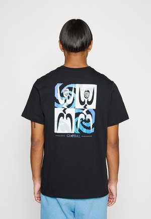 Personne avec des cheveux courts et foncés portant un T-shirt noir avec des motifs en spirale abstraits bleus et blancs et le texte "GLOBAL" dans le dos.
