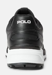 Černá atletická bota s texturovaným syntetickým svrškem, bílými doplňky a polstrovaným límcem. Má pevnou černou gumovou podrážku a detail s logem.