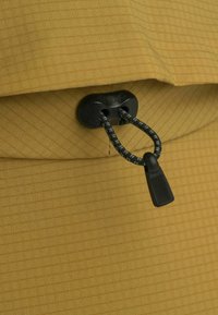 Tela amarilla con un sutil patrón de cuadrícula, que presenta un botón de plástico negro y una cuerda para el ajuste. Textura suave, diseño minimalista.