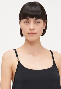 Top negro sin mangas con tirantes ajustables. Presenta herrajes plateados en el tirante izquierdo. Textura de tela suave, diseño ajustado y un sutil brillo.