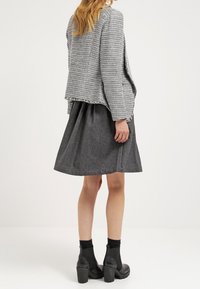 Blazer gris texturizado sobre una falda negra en línea A, combinado con botas negras hasta el tobillo. La tela está tejida con un patrón de pata de gallo.