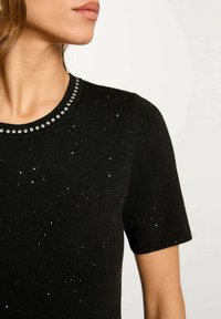 Maglietta nera a maniche corte in maglia con scollatura rotonda decorata da stud in tonalità argento e punteggiata di glitter metallici su tutto il tessuto.