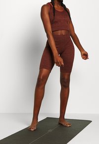 Bordeaux sportset bestaande uit een cropped tanktop en hoog getailleerde shorts, gemaakt van een gestructureerd materiaal. Model staat op een yogamat.