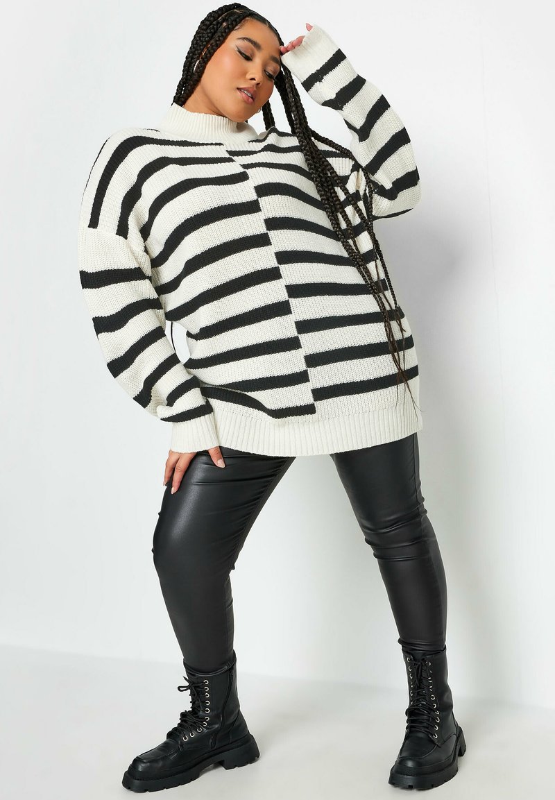 Gestreifter Pullover in Schwarz-Weiß mit hohem Ausschnitt, oversized Passform und gerippten Bündchen. Kombiniert mit glänzenden schwarzen Leggings und Kampfstiefeln.