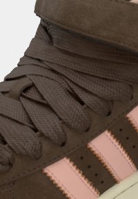 Καφέ σουέτ αθλητικό παπούτσι με υφασμένες κορδόνες, ροζ ρίγες στο πλάι και μαξιλαρωτό περιμετρικό μέρος στον αστράγαλο. Διαθέτει λείο πέλμα σε κρεμ απόχρωση.