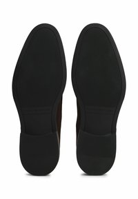 Suelas de zapatos negras con una superficie texturizada, fabricadas con un material de caucho y un sutil detalle de marca a lo largo del costado.